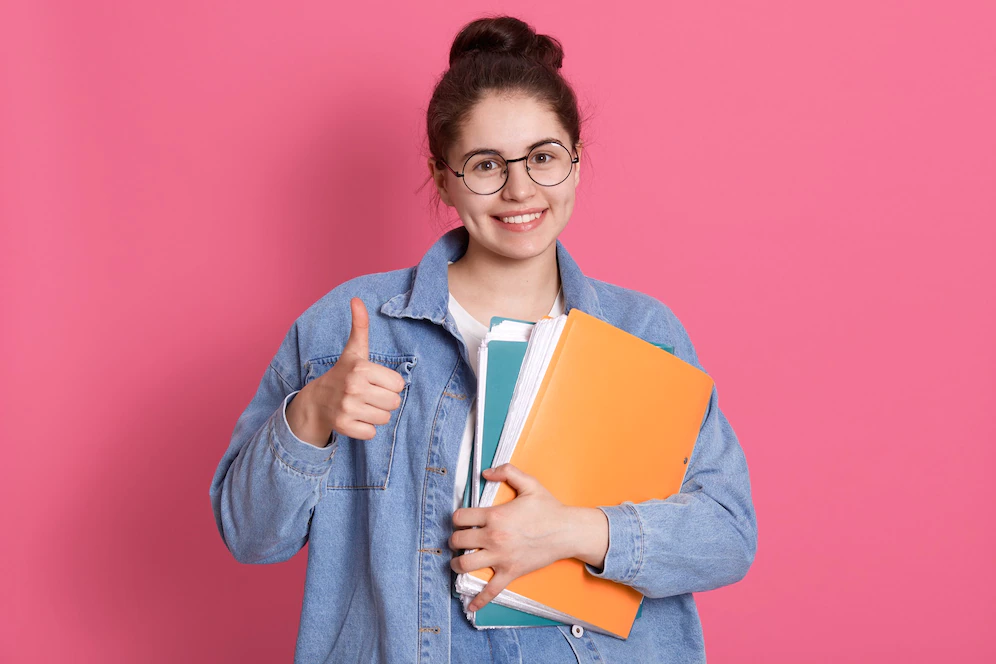 young-student-woman-wearing-denim-jacket-eyeglasses-holding-colorful-folders-showing-thumb-up-pink_176532-13861